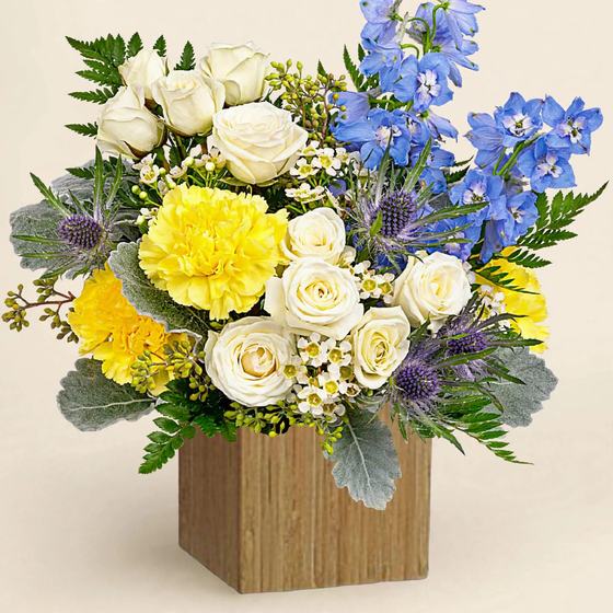Blue Meadow Garden Box with white and yellow roses, blue delphinium and thistles in a wooden box on a cream background