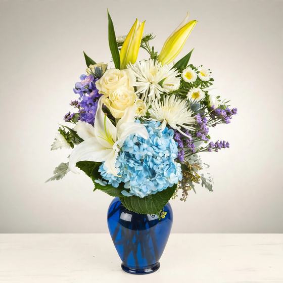 Blue Serenity Bouquet with blue hydrangea, white lilies and yellow lilies in a cobalt vase on a cream background