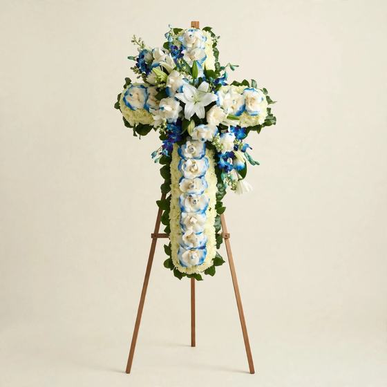 Blue Serenity Cross with white lilies, blue-tipped roses and blue delphinium displayed on a tall wooden easel