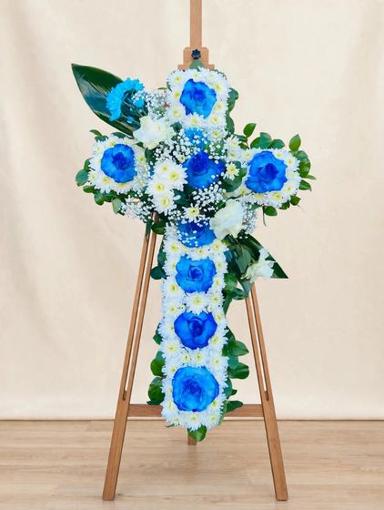 Standing cross spray with blue and white roses, white daisies and baby's breath on a cream background