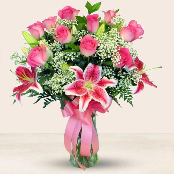 Pink roses and pink lilies with a pink ribbon in a glass vase on a cream background
