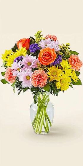 Orange roses, yellow and pink daisies, and peach carnations in a glass vase