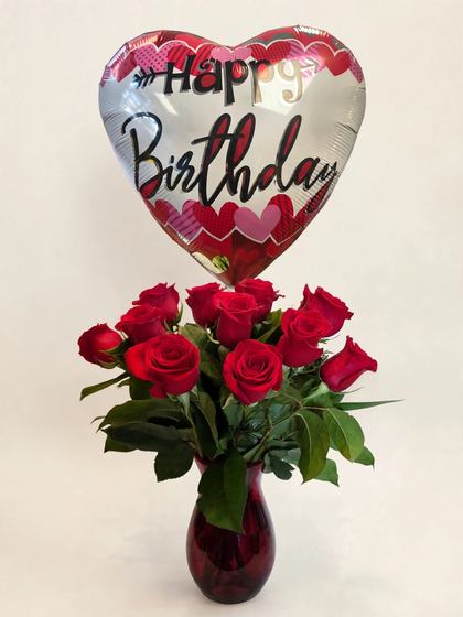 A dozen red roses in a glass vase with a Happy Birthday balloon
