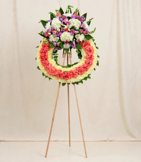 Funeral wreath with a ring of coral roses, white hydrangeas, pink roses and purple blooms on a cream background