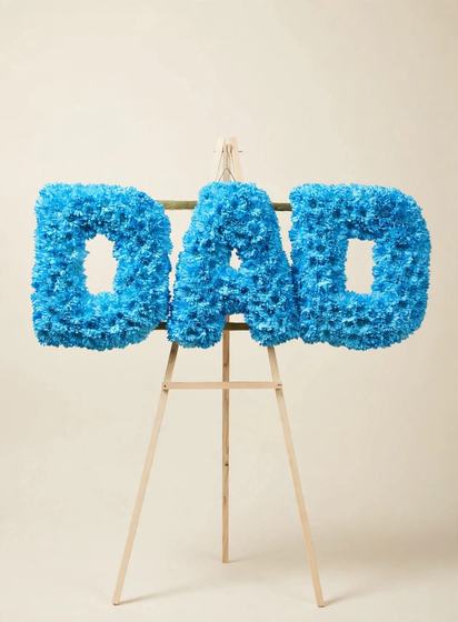 DAD Funeral Letters made of blue cushion daisies displayed on a wooden easel