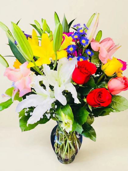Fiesta Bloom Bouquet with yellow lilies, red and pink roses, white lilies and blue asters on a cream background