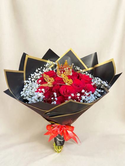 Two dozen red roses with baby's breath, a golden crown and golden butterflies in black wrap with gold trim and a red bow on a cream background