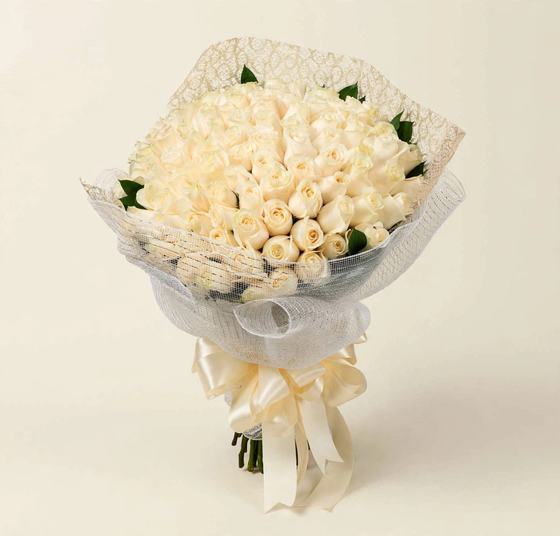 Fifty white and cream roses in white mesh wrap with an ivory bow