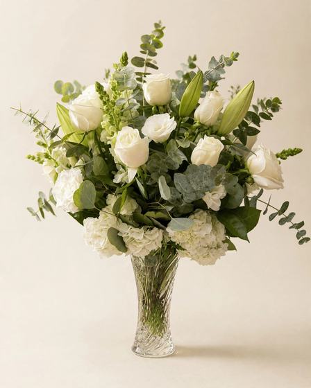 White roses, white hydrangea, lily buds, snapdragons and eucalyptus arranged in a cut crystal vase on a cream background