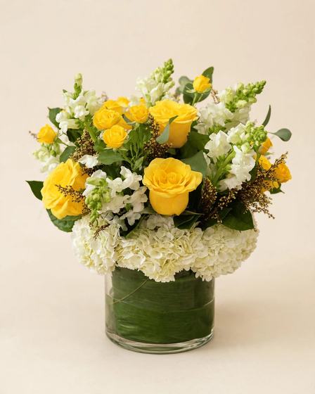 Yellow roses, white snapdragons, white hydrangea and eucalyptus in a glass cylinder