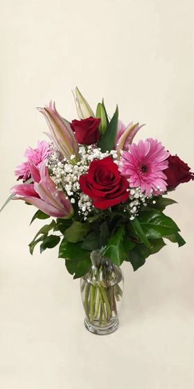 Red roses, pink lilies and gerberas with baby's breath in a glass vase