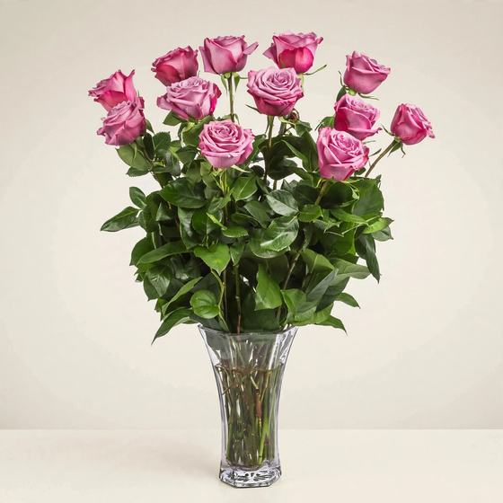 A dozen mauve-pink roses arranged in a cut crystal vase on a cream background