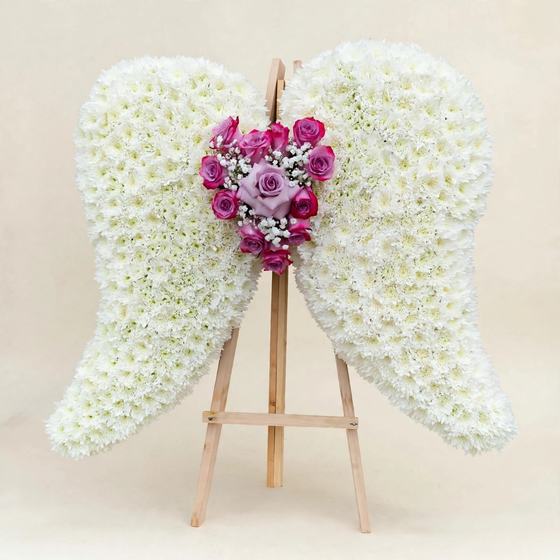 White floral angel wings tribute on a tall stand, cream studio background
