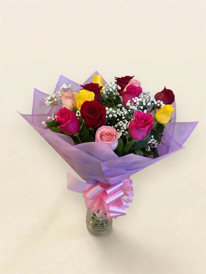 A dozen pastel mixed roses with baby's breath in lavender wrap with a pink bow in a glass vase on a cream background