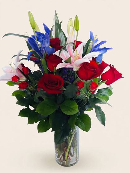 Red roses, pink and white stargazer lilies, blue iris and red spray roses in a glass vase