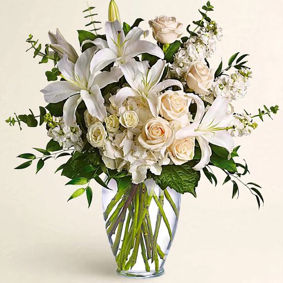 Peaceful White Garden with white lilies, white roses, white hydrangea and eucalyptus in a clear glass vase on a cream background