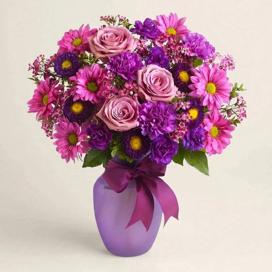 Purple Daisy Delight Bouquet with pink and purple daisies, lavender roses and purple carnations on a cream background