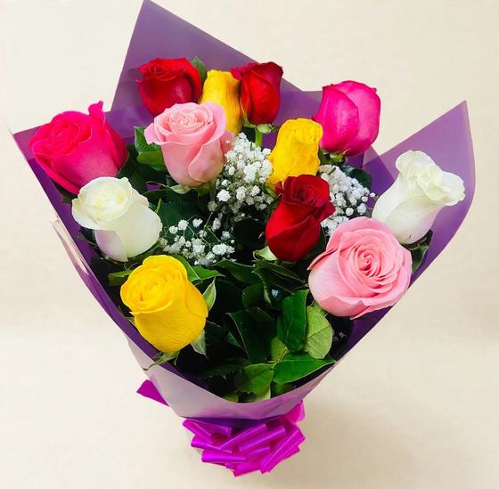 A dozen mixed roses in red, pink, yellow and white with baby's breath in purple wrap on a cream background