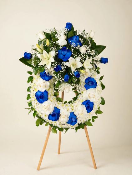 Royal Blue Wreath with blue roses, white roses, white lilies and white chrysanthemums in a round standing wreath on a tall wooden easel