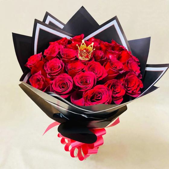 Two dozen red roses with a small gold crown in black wrap with white trim and a red ribbon on a cream background
