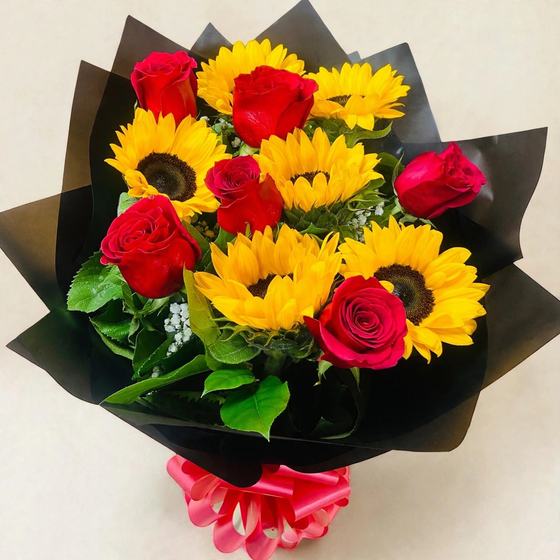 A dozen red roses and sunflowers with baby's breath in black wrap with a red bow on a cream background