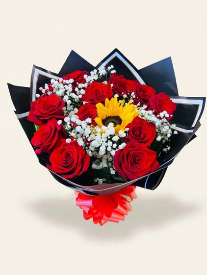 A dozen red roses with one sunflower and baby's breath in black wrap with white trim and a red bow on a cream background