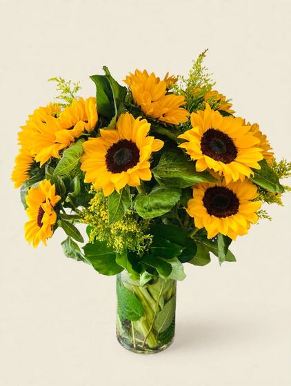 Bright yellow sunflowers with solidago and greenery in a clear glass vase