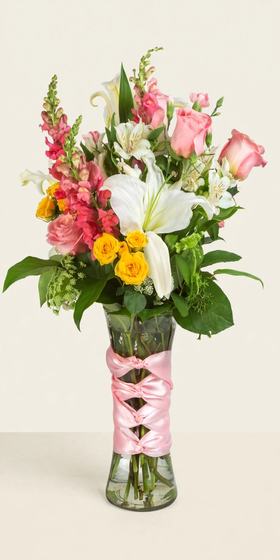 Sunset Blush Bouquet with pink and coral roses, white lilies, yellow spray roses and pink ribbon on a cream background
