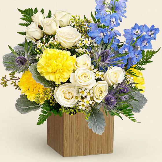 White roses, yellow carnations and blue delphinium in a wooden box