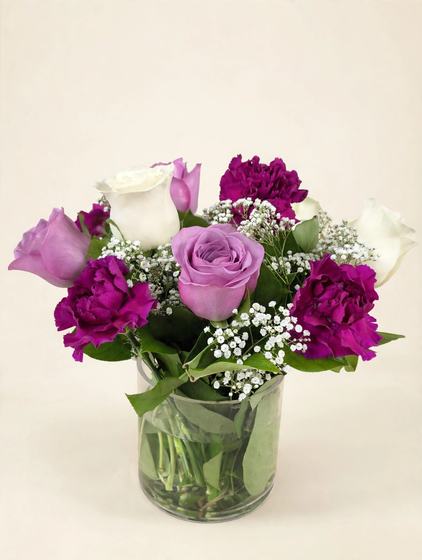 Purple, pink and white roses with magenta carnations and baby's breath in a glass vase on a cream background