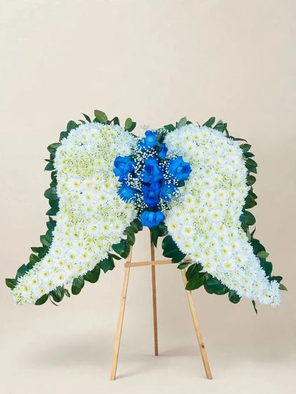 White angel wings made of white cushion daisies with blue roses at the center, displayed on a wooden easel