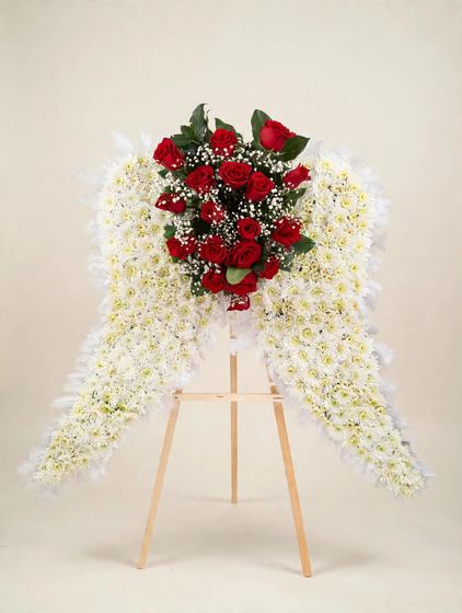 White angel wings made of white cushion daisies with a heart of red roses, displayed on a wooden easel